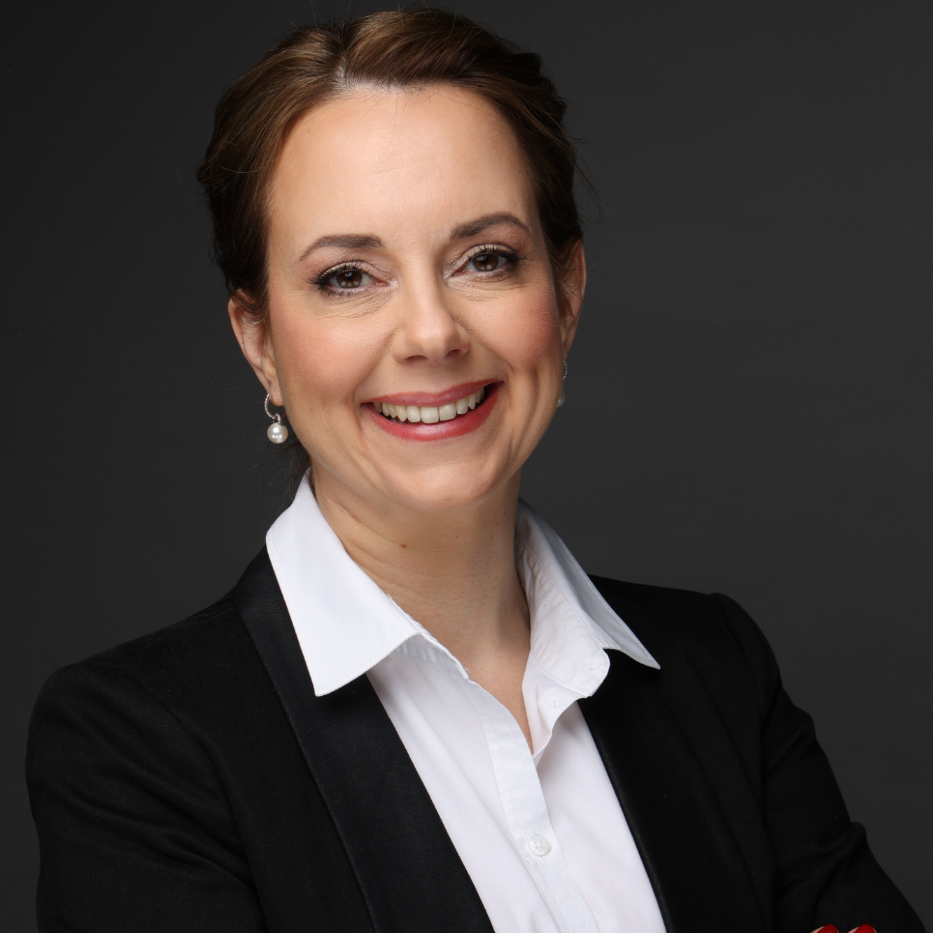 Frau mit einem freundlichen Lächeln, trägt einen schwarzen Blazer und ein weißes Hemd.